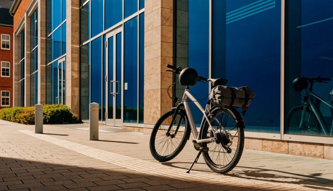 Modernes Pendler-/E-Bike als Dienstrad vor einem Bürogebäude, mit Helm am Lenker und Packtasche