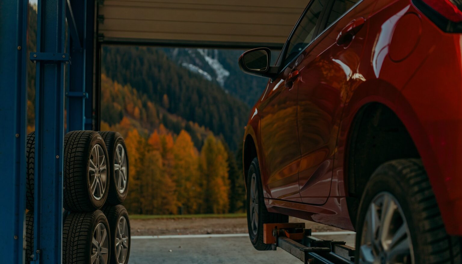 Reifen in Liezen: Winterreifen auf Alufelgen neben einem Auto auf der Hebebühne, im Hintergrund herbstliche Berge